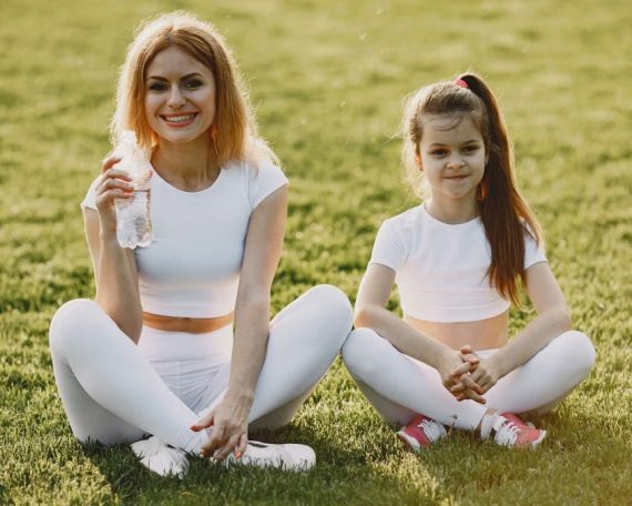 Smiling mother and daughter wearing matching outfits sitting on grass in a park.