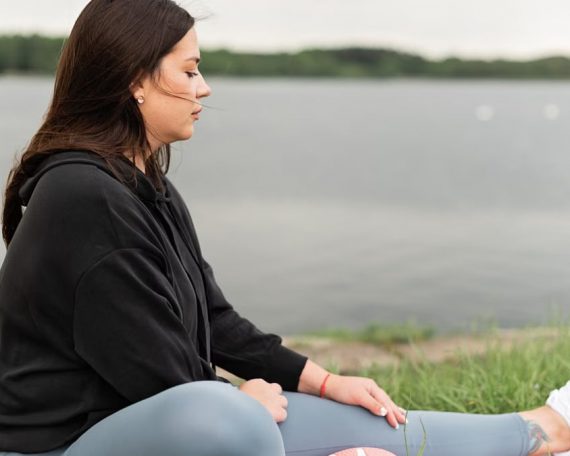 Woman meditating outdoors by a tranquil lakeside, fostering health and wellness.